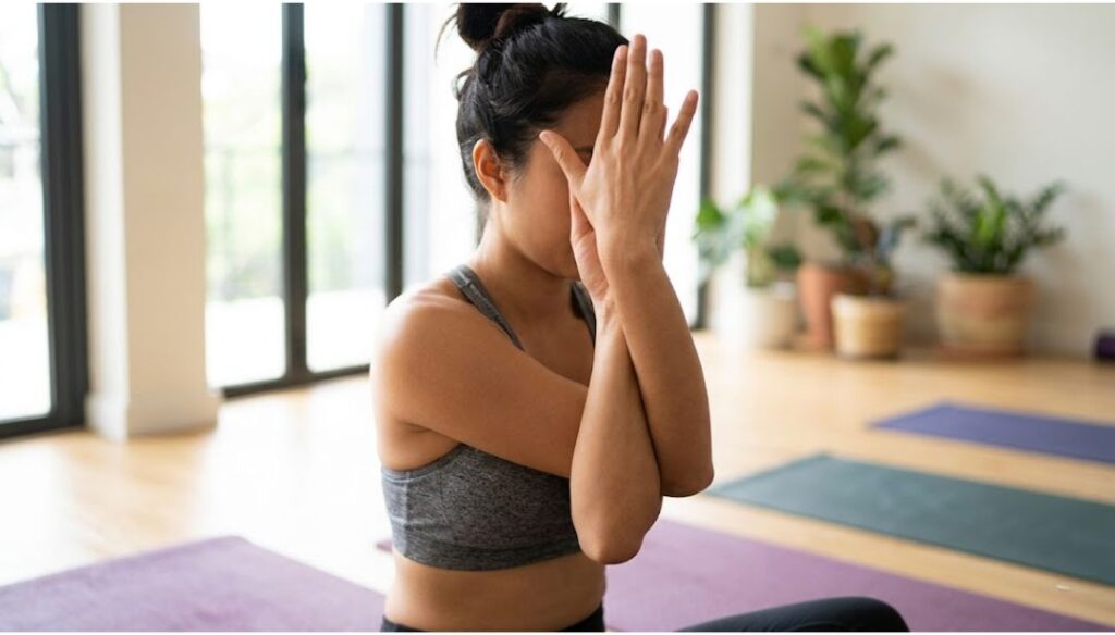Woman practicing Eagle Arms pose (Garudasana arms) in a yoga studio to improve shoulder flexibility and relieve upper back tension.